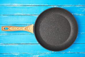 new empty frying pan with a brown handle on a blue wooden background photo