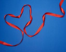 red silk thin ribbon twisted on a blue background photo