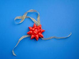 golden silk thin ribbon twisted and red shiny bow on a blue background photo