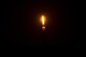 Single burning candle flame or light glowing on an orange candle on black or dark background on table in church for Christmas, funeral or memorial service photo