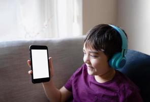 Kid showing mobile screen and using mobile phone searching information on internet for homework,Child wearing headphone listening to music,Home schooling,E-learning education,Children with technology
