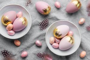 Easter eggs are painted with violet and gold paint on a gray linen background.