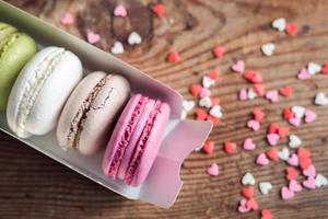 macarons variados en una caja salpicada de pequeños corazones sobre un fondo de madera, vista superior foto