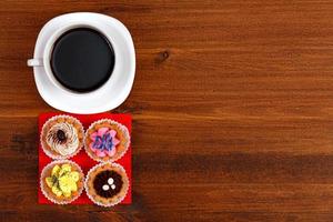 Cup of tea or coffee and four cupcakes on brown table. Top veiw photo