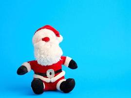 traditional toy santa claus in a red suit and white beard sits on a blue background photo