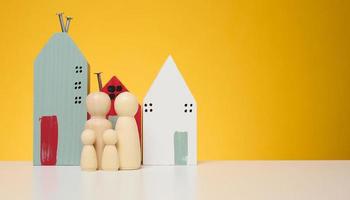 Wooden house and miniature figurines of a family on a yellow background. The concept of selling and buying real estate photo