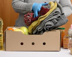 woman in gloves keeps collecting food, fruits and things and a cardboard box for helping those in need photo