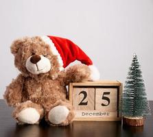 oso de peluche marrón con sombrero rojo, calendario de escritorio de madera con fecha 25 de diciembre foto