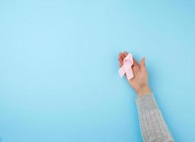 female hand holds a pink bow-shaped ribbon on a blue background photo