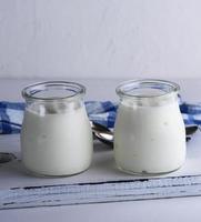 yogur casero en un frasco de vidrio sobre una tabla de madera blanca foto