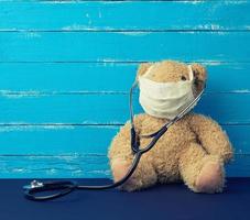 el oso de peluche está sentado con una máscara médica blanca, el estetoscopio negro cuelga de su cuello foto