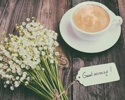 cup of hot black coffee and a bouquet of fresh lilies of the valley photo