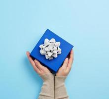 two female hands in a sweater hold closed square blue box with a bow photo