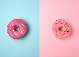 two whole round pink donuts with colored sprinkles lie on a blue-pink background photo