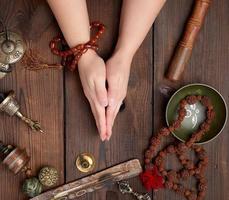 dos manos en una pose de oración sobre una mesa marrón de madera en medio de herramientas antiguas de meditación tibetana foto