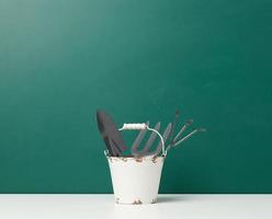 Miniature garden tools in a metal bucket on a green background photo