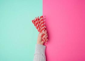 hand holds a stack of red paper tubes for a cocktail on a multi-colored background photo