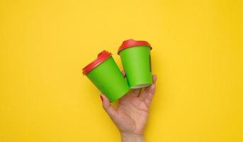 female hand holding disposable green paper cup on a yellow background photo