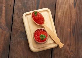 el caviar rojo de salmón rosado se encuentra en una cuchara de madera sobre una tabla para cortar. mesa de madera marrón foto