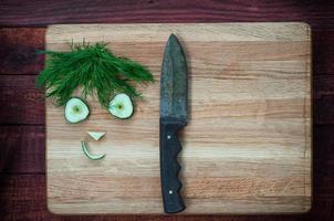 caras graciosas de rodajas de pepino y eneldo en la tabla de cortar con un cuchillo foto