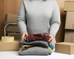 woman in a gray sweater collects clothes in a box, concept of assistance and volunteering, moving photo