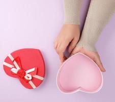 two hands hold a paper open red box in the shape of a heart on a purple background photo