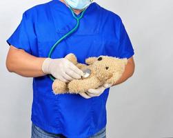 doctor in blue uniform and white latex gloves holding a brown teddy bear photo