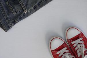 pair of red sneakers and a fragment of blue jeans on a white wooden background photo