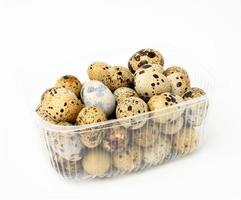 a bunch of raw quail eggs in a plastic transparent container on a white background, diet food photo