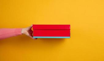 female hand holding a red cardboard box on a yellow background, delivery photo