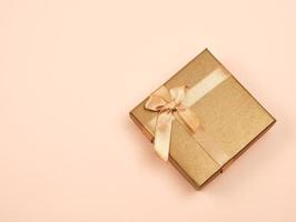 closed golden gift box with a bow on a beige background photo