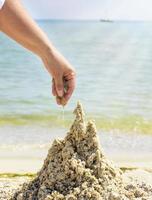 mano femenina construye un castillo de la arena mojada del mar foto