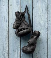 pair of very old leather black boxing gloves hanging on a nail photo