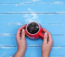 taza roja con café negro caliente en manos femeninas foto