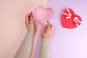 two hands hold a paper open red box in the shape of a heart on a purple background photo