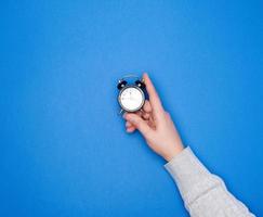 hand with a gray sweater holds a round black alarm clock photo