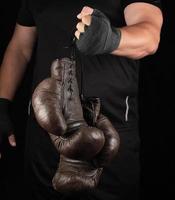 athlete in black clothes holds very old vintage leather black boxing gloves photo