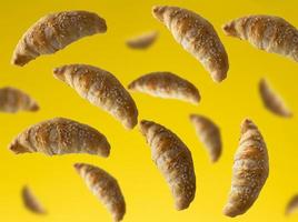 flying mini croissants sprinkled with sesame seeds on a yellow background photo