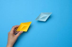 A woman's hand holds a yellow paper boat, next to it is blue. photo