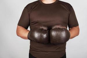 man stands wearing very old vintage brown boxing gloves on his hands photo