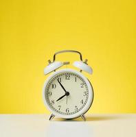 round white alarm clock, five minutes to eight in the morning. Yellow background photo