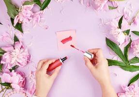 female hands with smooth fair skin keep liquid red lipstick in a tube photo