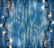 two wires of electric garland with small glowing light bulbs in the old blue wooden background photo