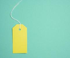 Empty yellow cardboard tag on a white rope, green background. Price tag template photo