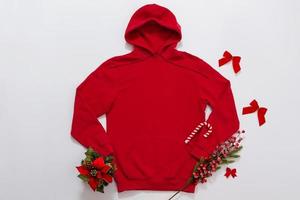 Close up red blank template hoodie copy space. Christmas Holiday concept. Top view mockup hoodie, scarf, hat. Red holidays decorations white background. Happy New Year accessories. Selective focus photo