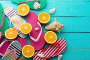 Summer fun time and flip flops. Sea shell. Slippers and orange fruit on blue wooden background. Mock up and picturesque. Top view. Copy space photo