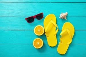 Yellow flip flops, red sunglasses, shell and orange fruit on blue wooden background. Top view and summer time. photo
