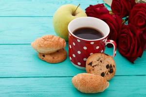 Cup of coffee with croissants and cookies and red roses on blue wooden background. Copy space. Mock up. Top view. Valentine mother day. photo