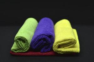 Multicolored towels on a black background. Terry towels. Colored rags in rolls. Rolled-up rags. photo