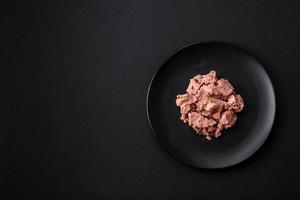 Delicious canned tuna meat on a black ceramic plate on a dark concrete background photo